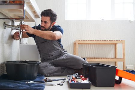 Male Plumber Working To Fix Leaking Sink In Home Bathroom